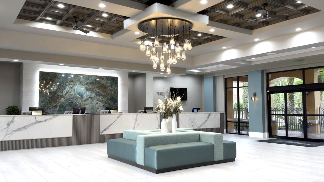 Modern hotel lobby with a central seating area, chandelier, and stylish reception desk.