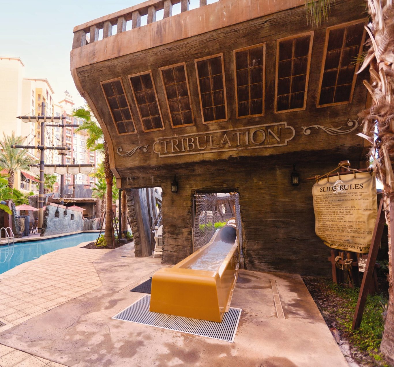 A golden water slide in a tropical resort, with a pirate ship theme nearby.