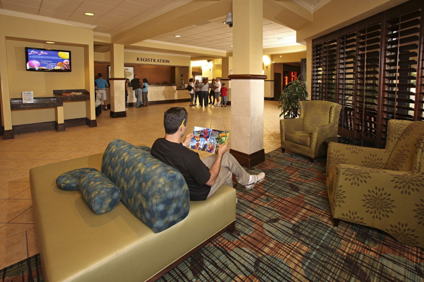 A person sits on a sofa in a hotel lobby, with seating and a reception area visible.