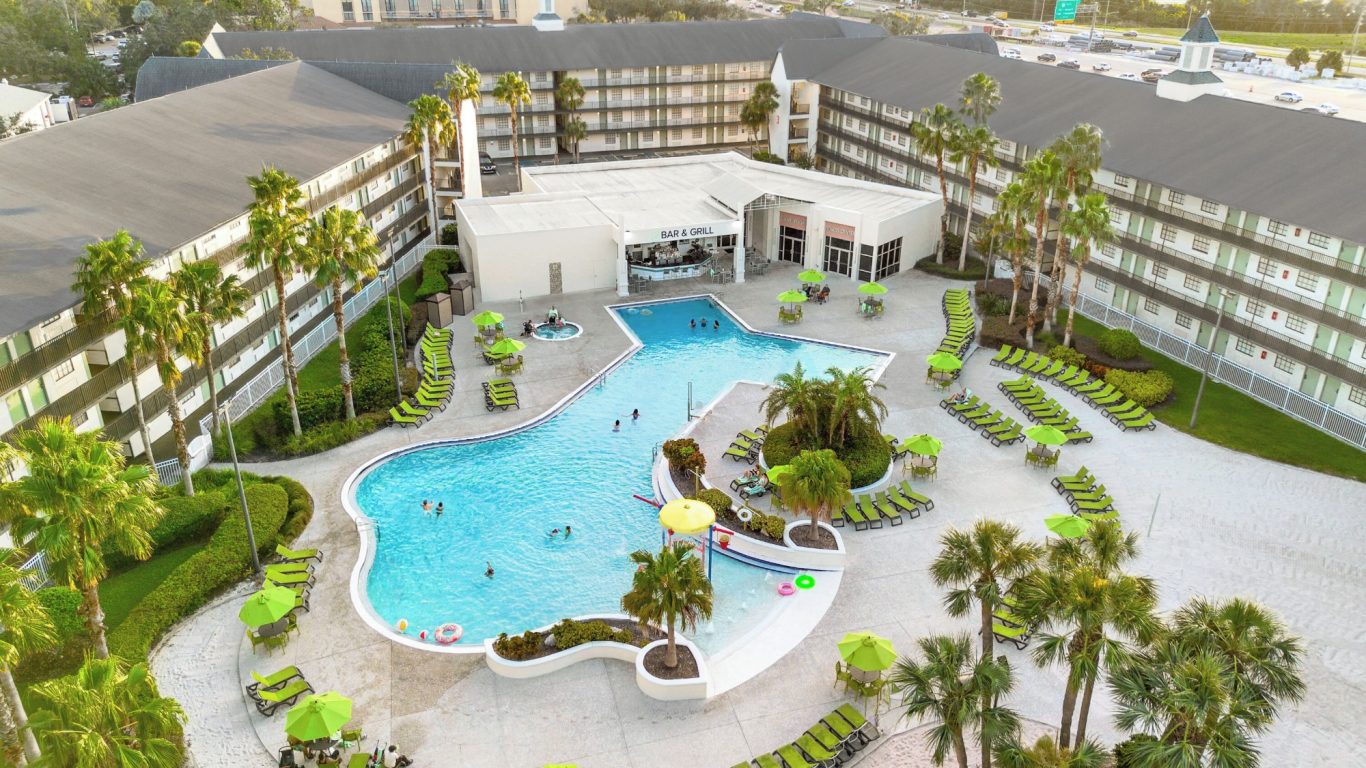 Hotel complex with a large pool surrounded by palm trees and sun loungers.