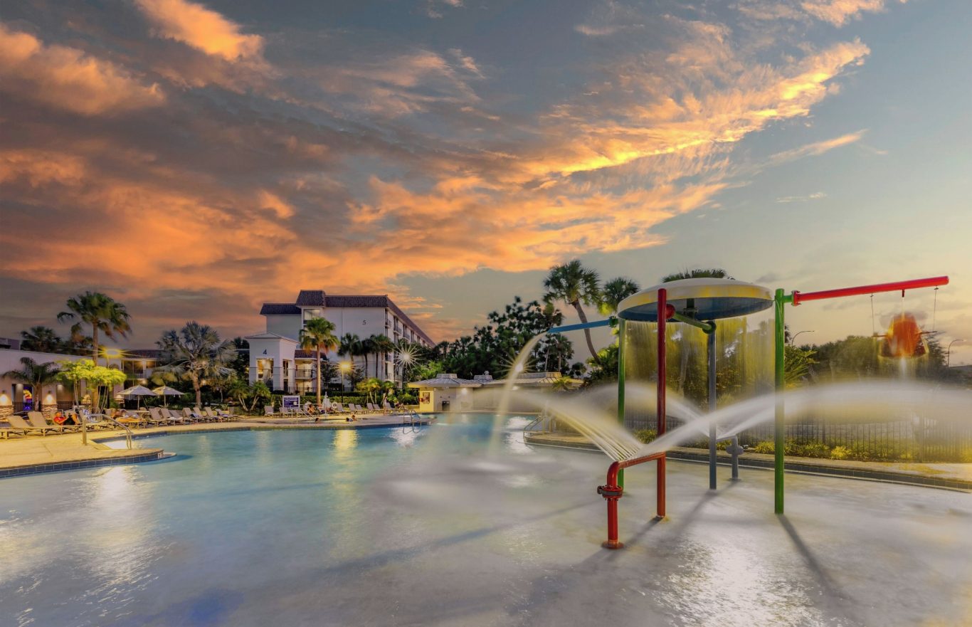 Water play area with colourful structures and a sunset sky in the background.