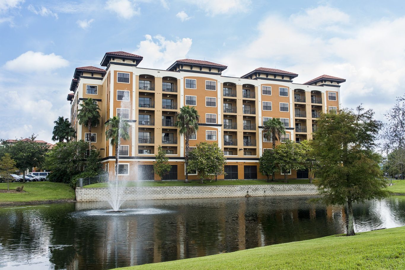 A modern building with orange exterior beside a pond and fountain, surrounded by trees.
