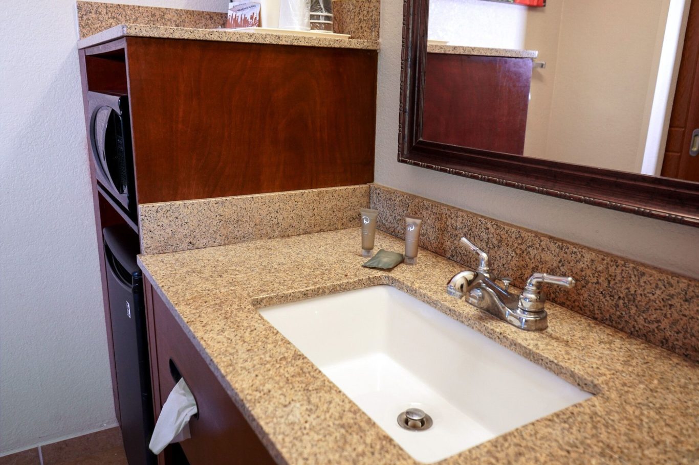 Modern bathroom sink with granite countertop, mirror, and wooden cabinetry.