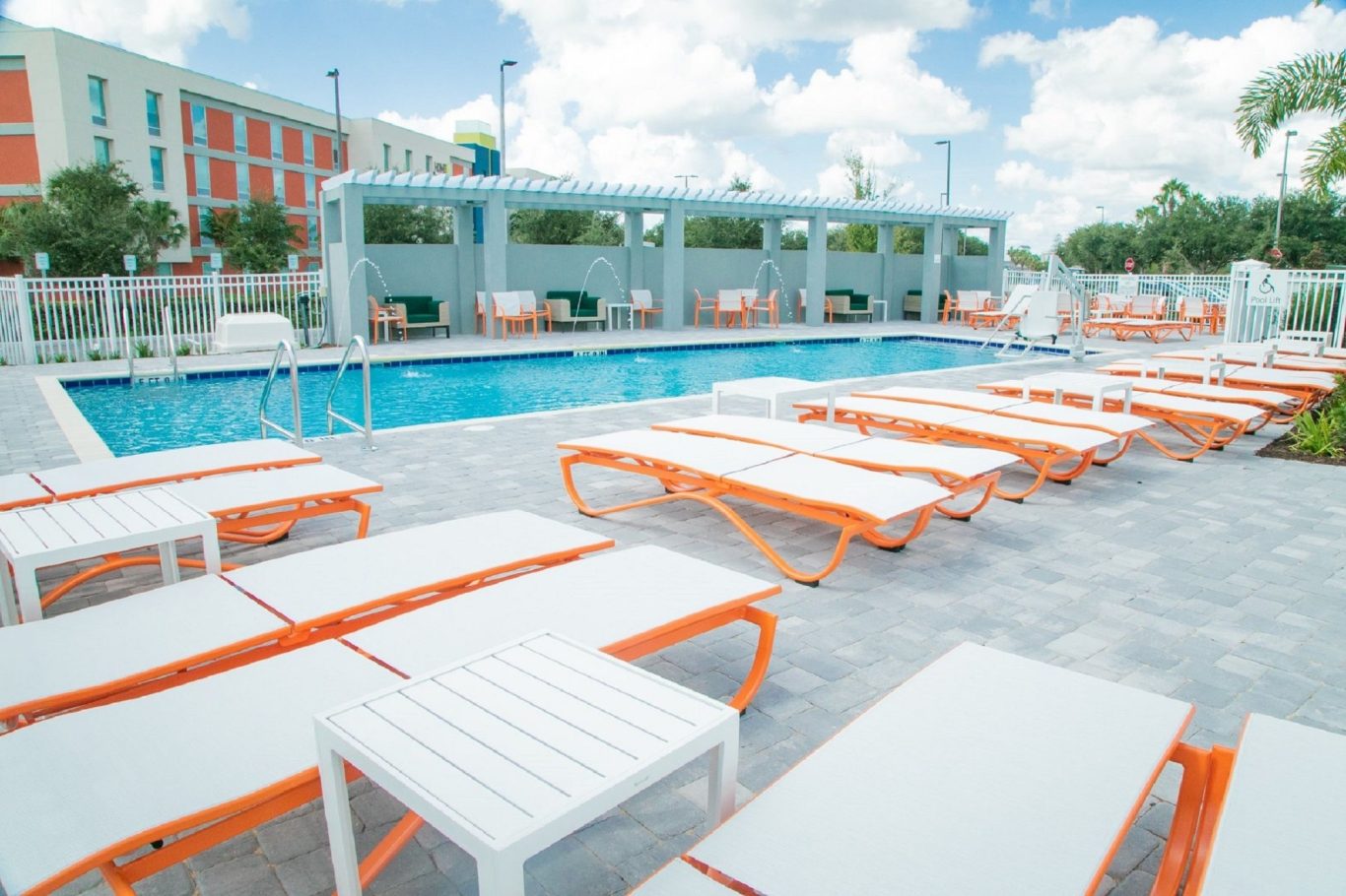 Pool area featuring orange and white loungers under a sunny sky.