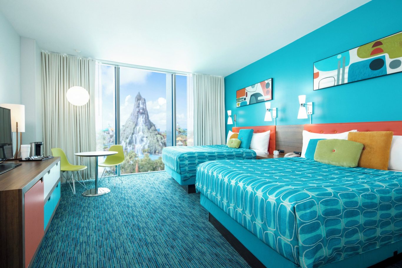 Brightly decorated hotel room with two beds and a view of a city skyline.