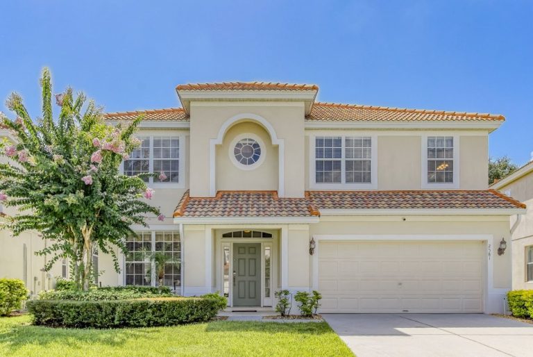 A modern two-storey house with a circular window, palm trees, and a well-maintained lawn.