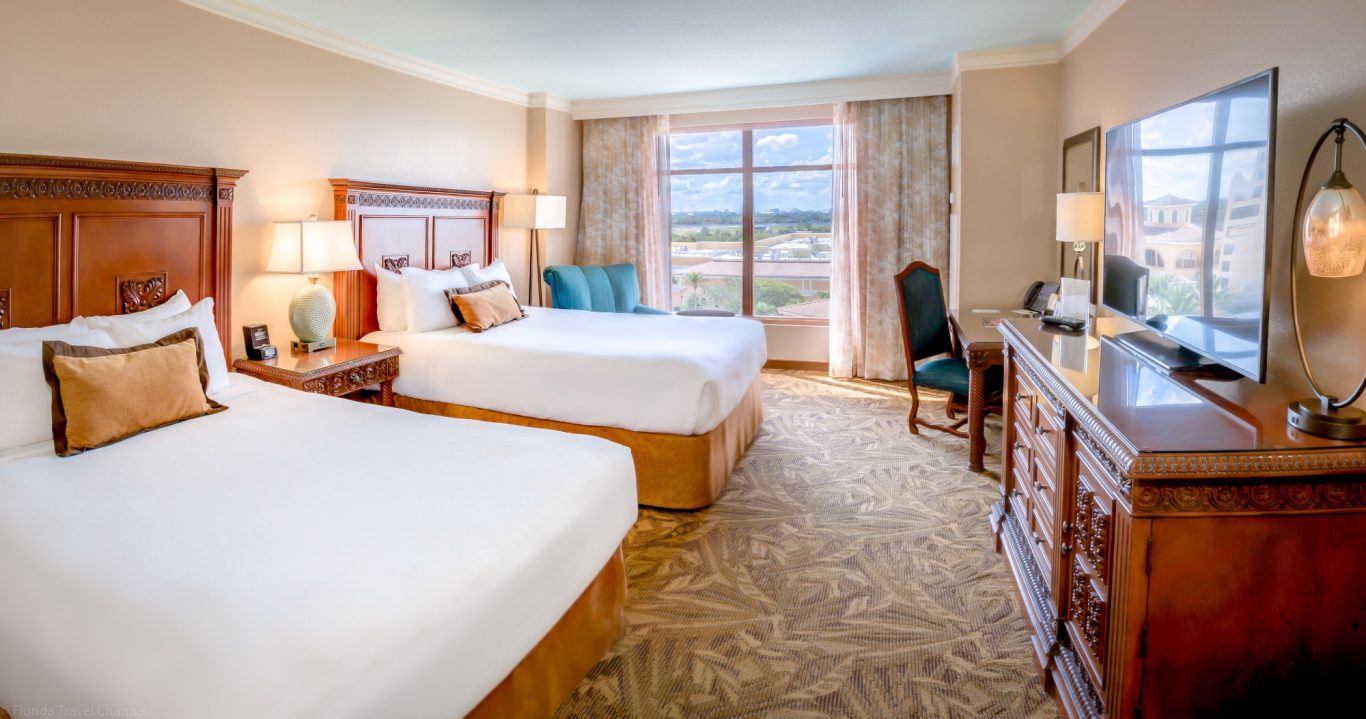Hotel room with two beds, a desk, and large windows offering a view.