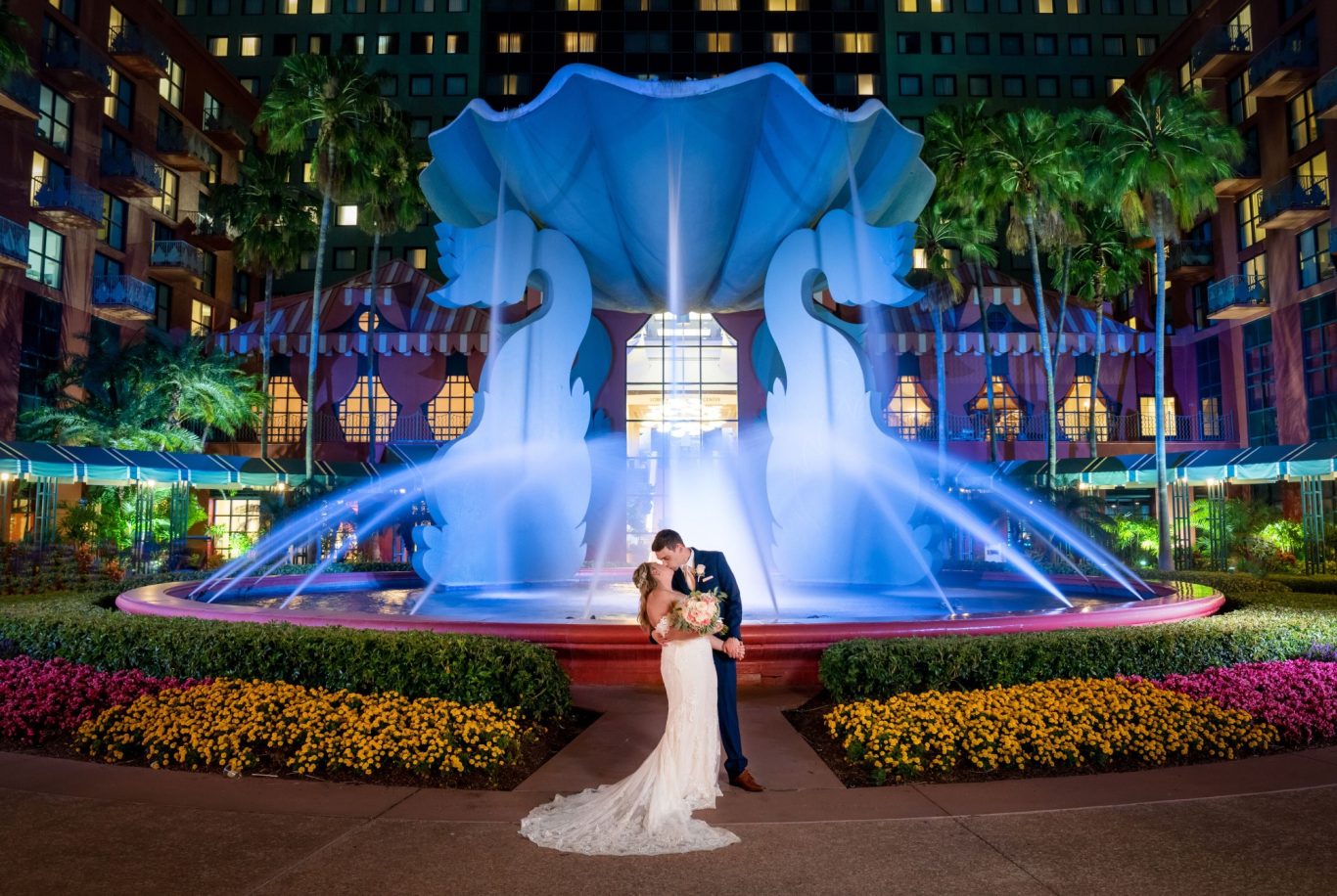 A couple shares a romantic moment in front of a vibrant fountain at night.