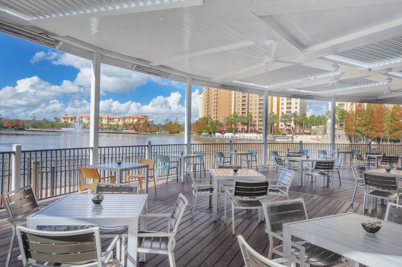 Modern outdoor dining area with tables overlooking a scenic waterfront and buildings.
