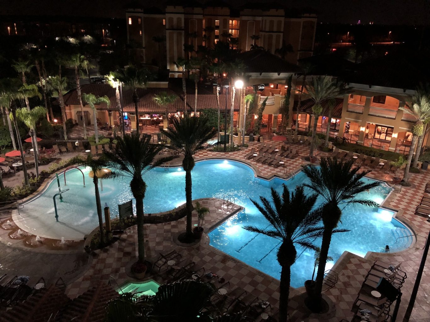 Nighttime view of a pool area surrounded by palm trees and lit pathways.