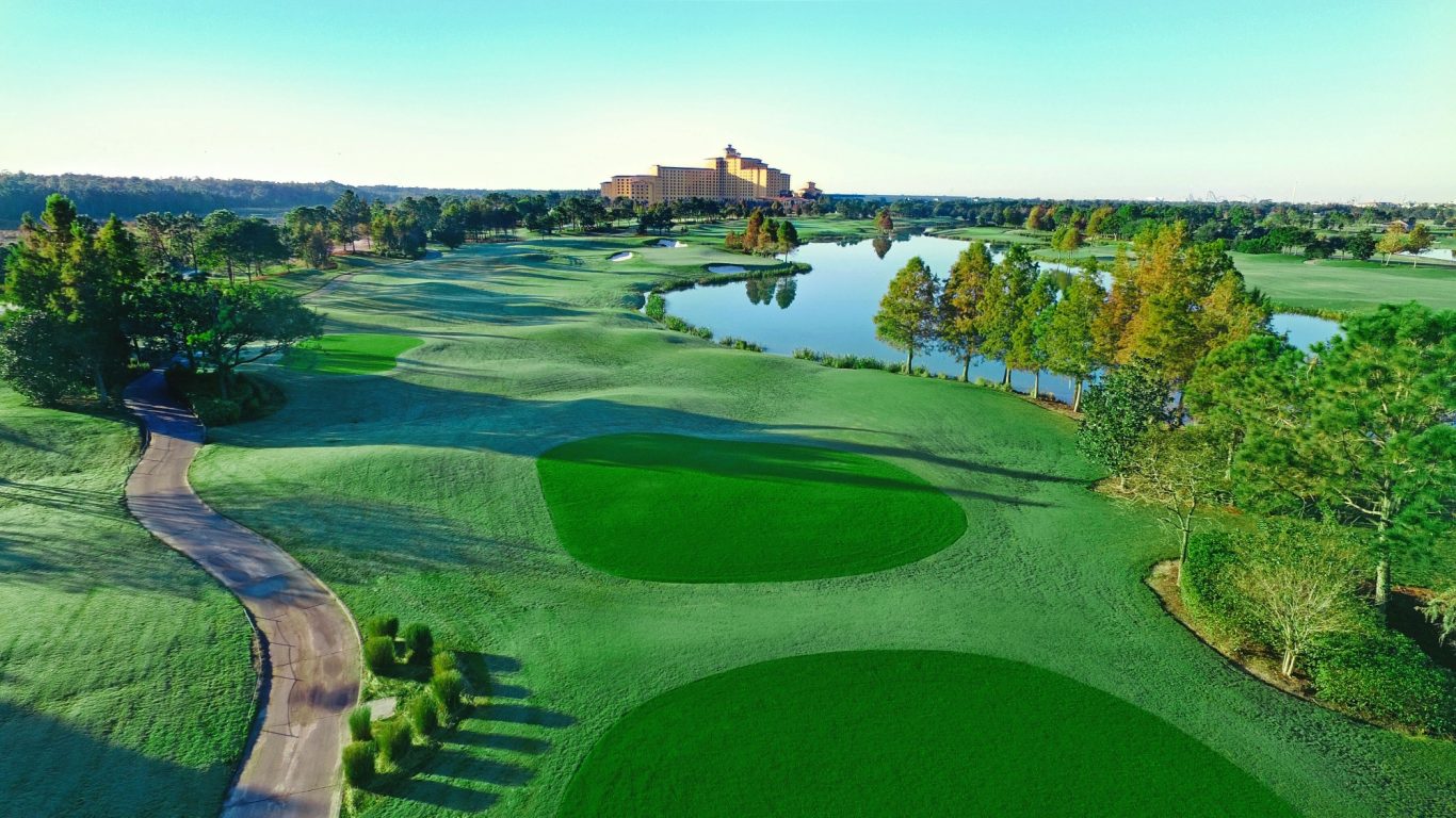 A scenic golf course with lush green fairways and a pond, surrounded by trees.