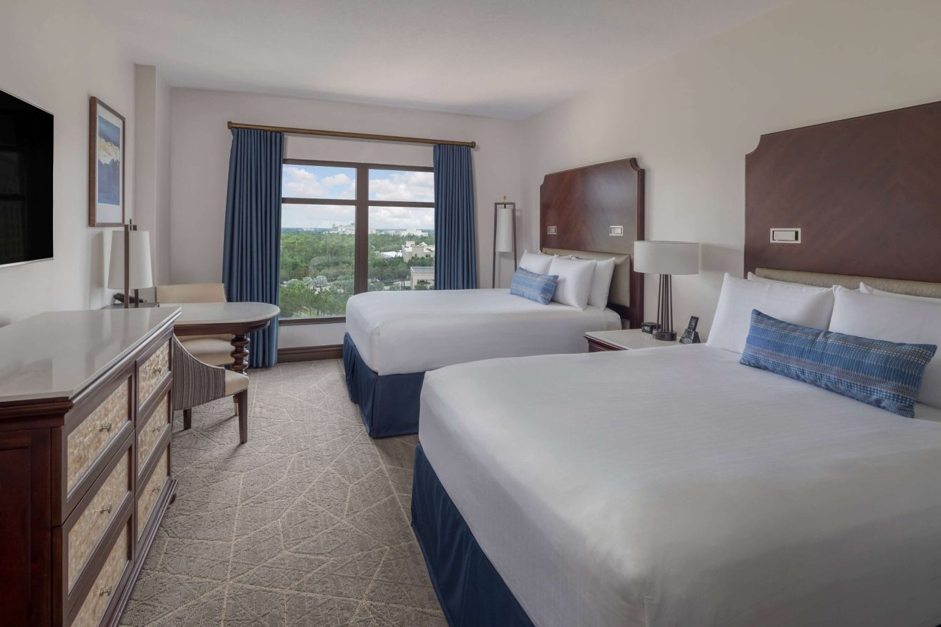 Hotel room with two double beds, a desk, large window, and light blue curtains.