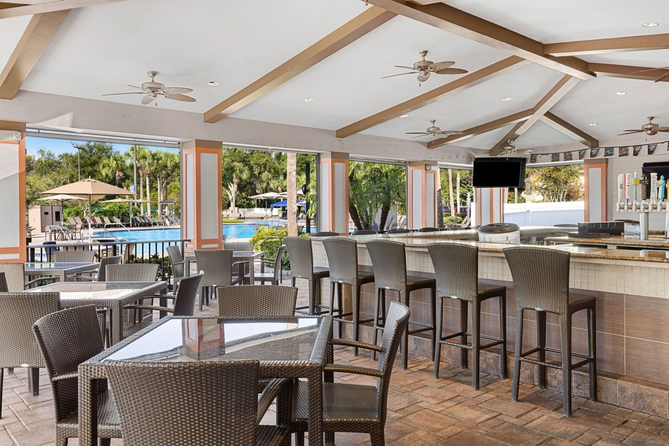 Modern bar area with high stools, tables, and a view of the pool outside.
