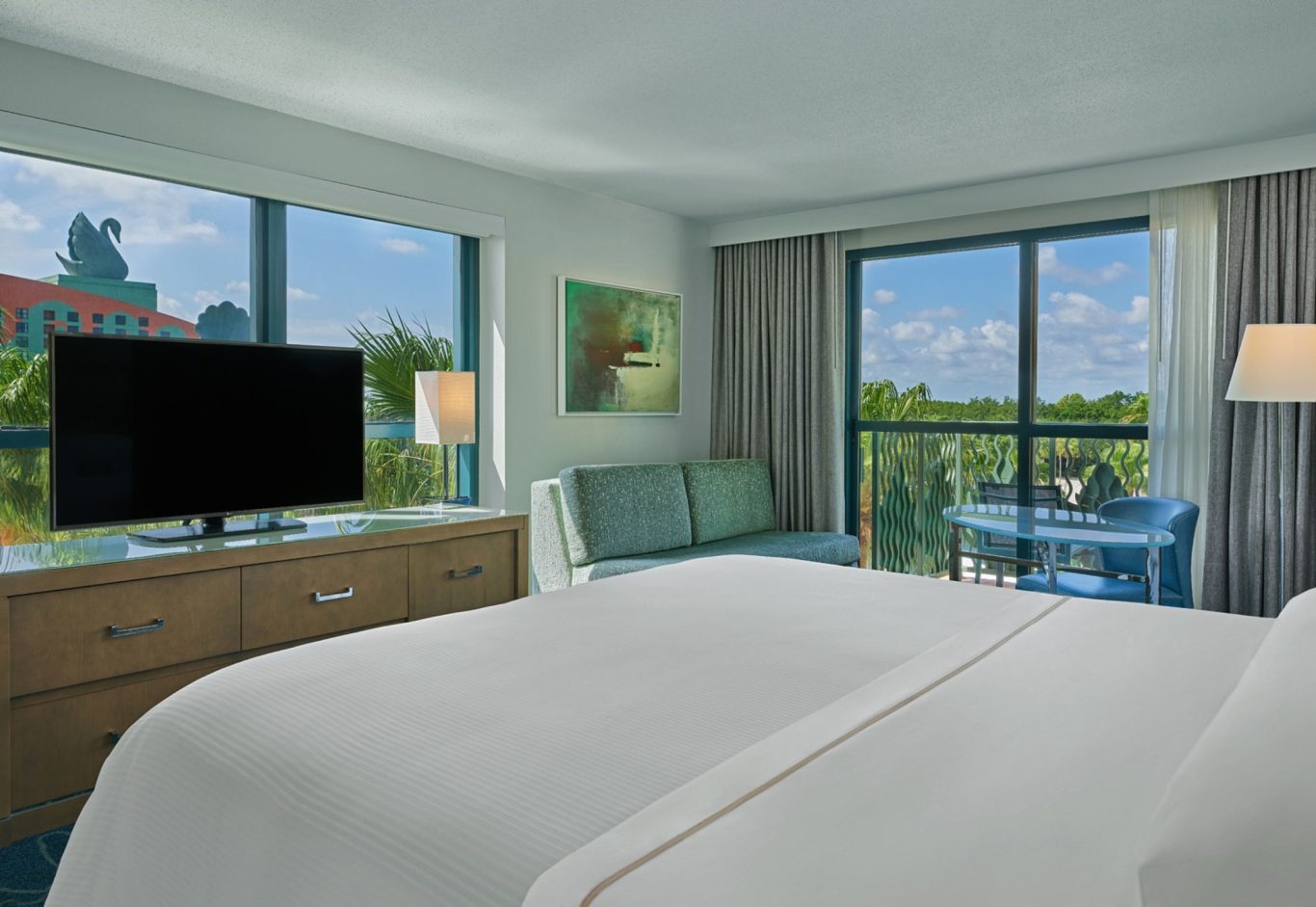 Modern hotel room with a king-size bed, large windows, and a view of greenery.
