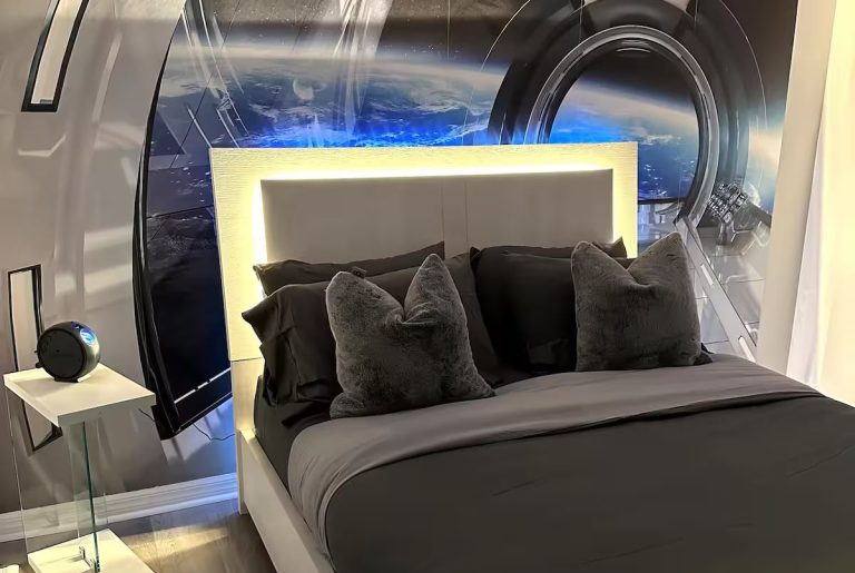 Modern bedroom with a padded headboard, grey bedding, and a space-themed mural.