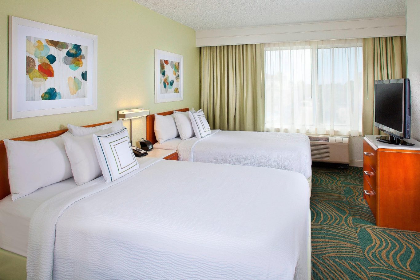 A bright hotel room with two double beds and large windows letting in natural light.