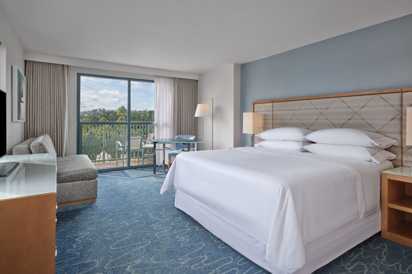 A bright, modern hotel room with a king-size bed and large windows offering a scenic view.