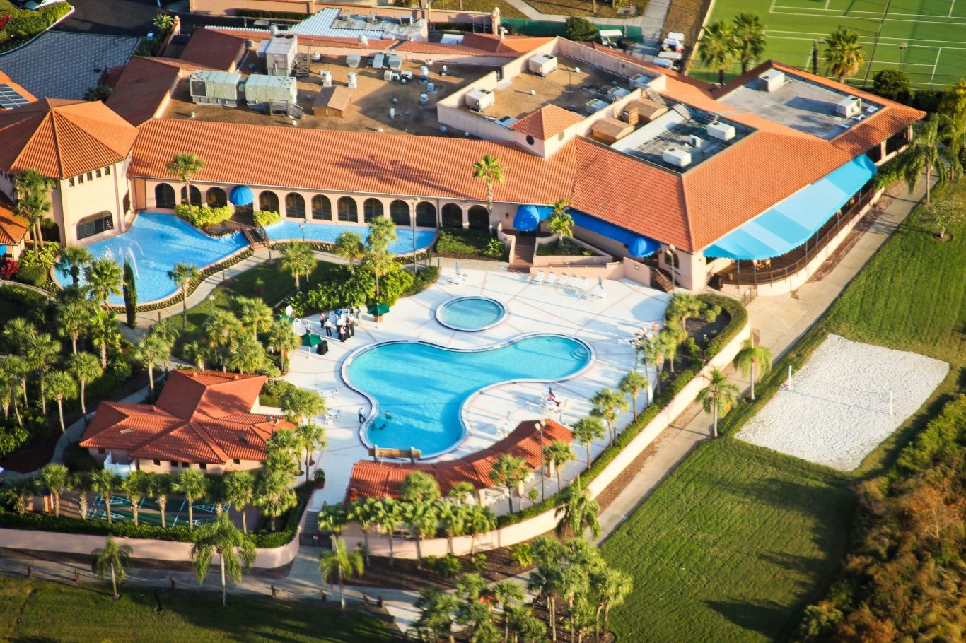 Aerial view of a resort with pools, palm trees, and a surrounding landscape.