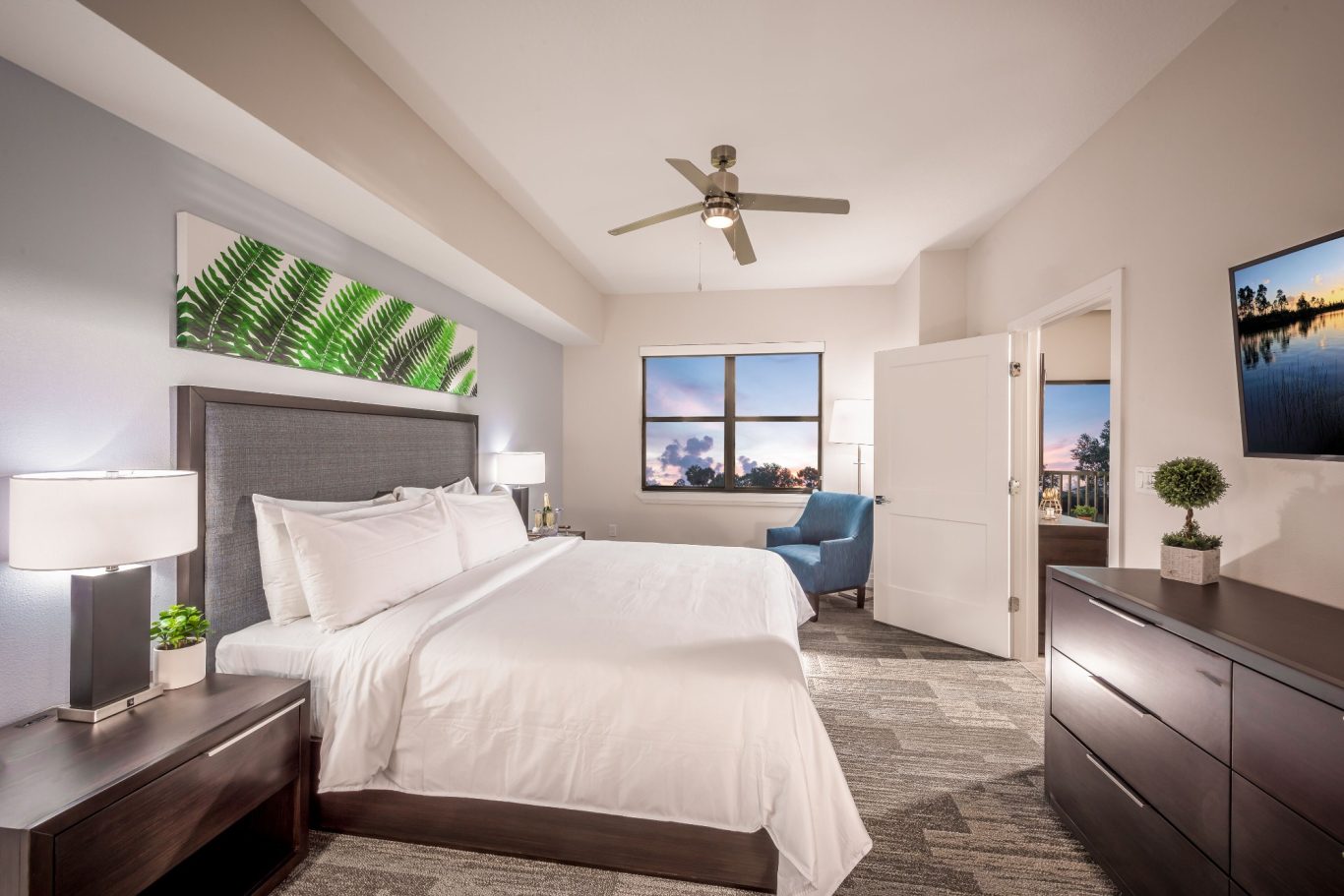 Modern hotel room with a king-size bed, seating area, and large windows.