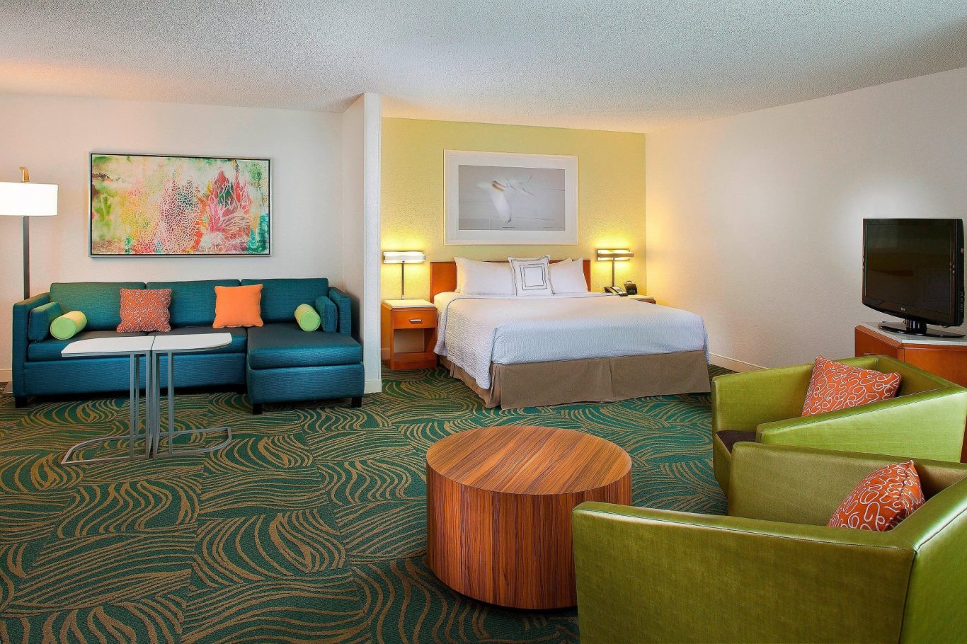 Spacious hotel room with a king bed, seating area, and vibrant decor.