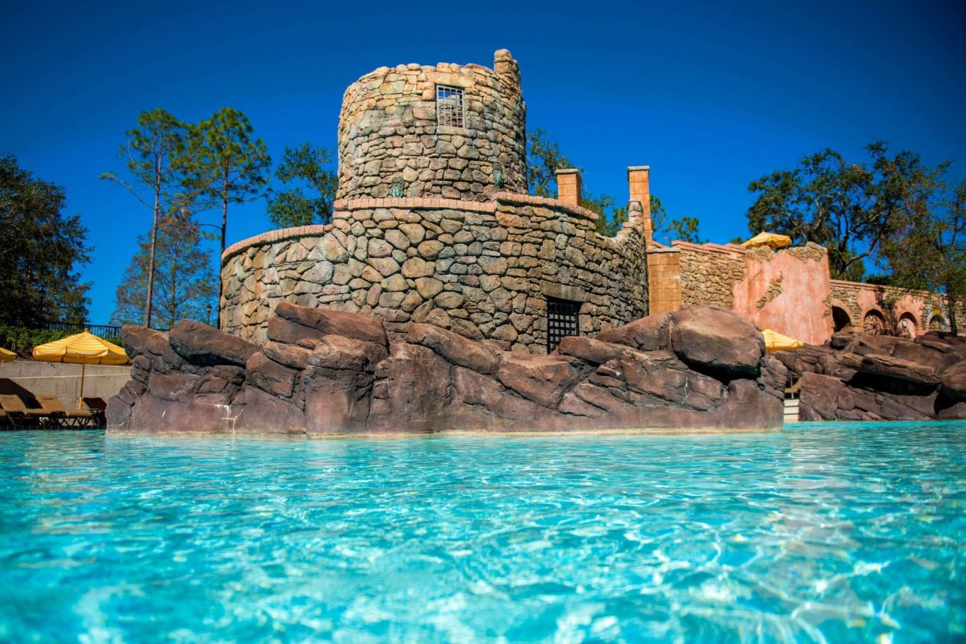 Stone tower beside a clear blue pool, with lush greenery in the background.