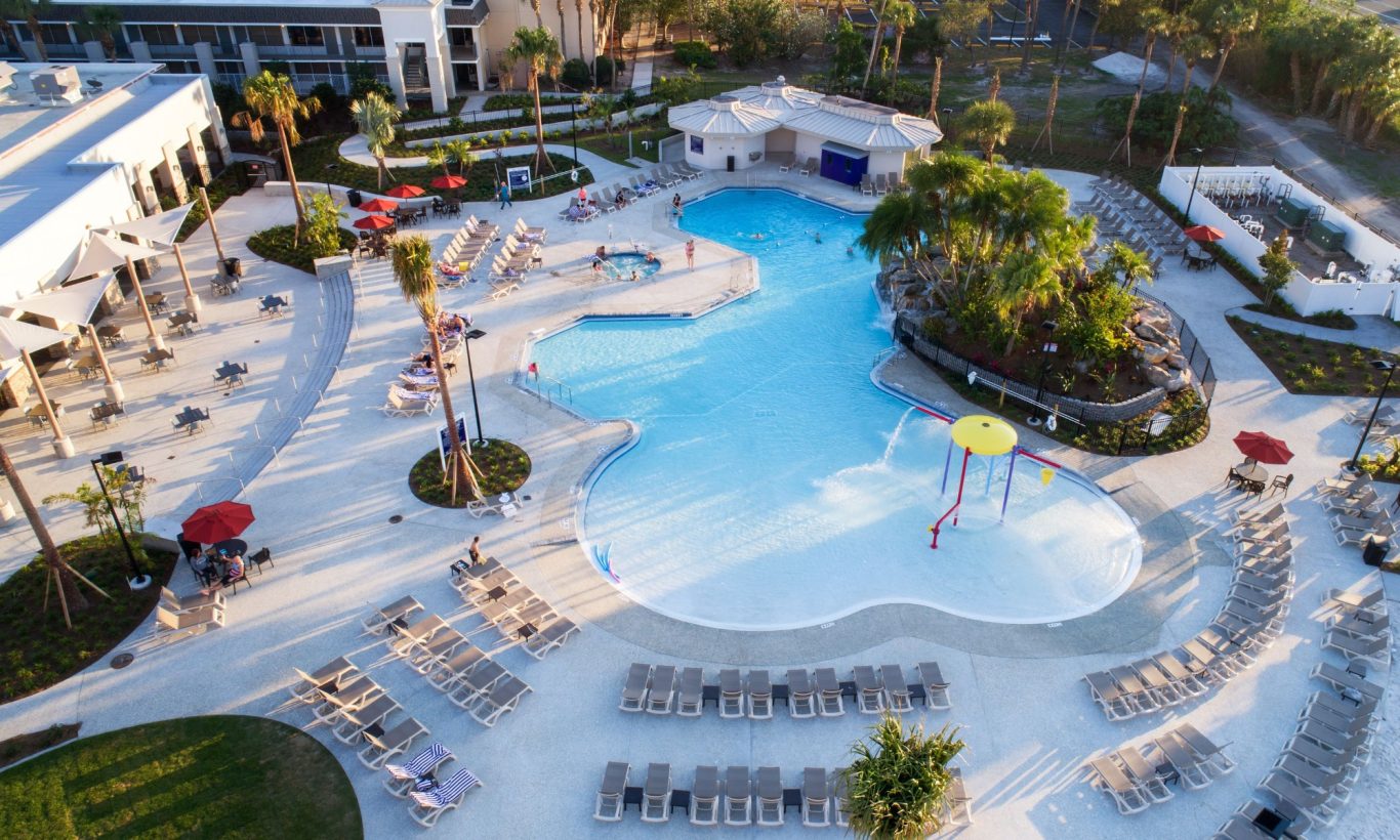 Aerial view of a resort pool surrounded by sun loungers and palm trees.