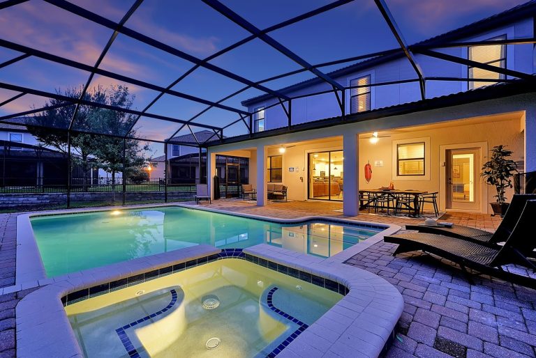 Modern backyard with a pool and hot tub, surrounded by a screened patio at dusk.
