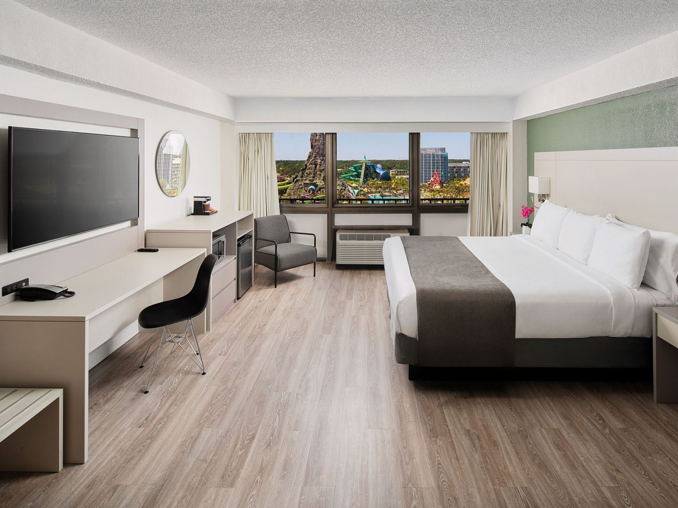 Modern hotel room with a king-size bed, desk, chair, and large window offering a city view.