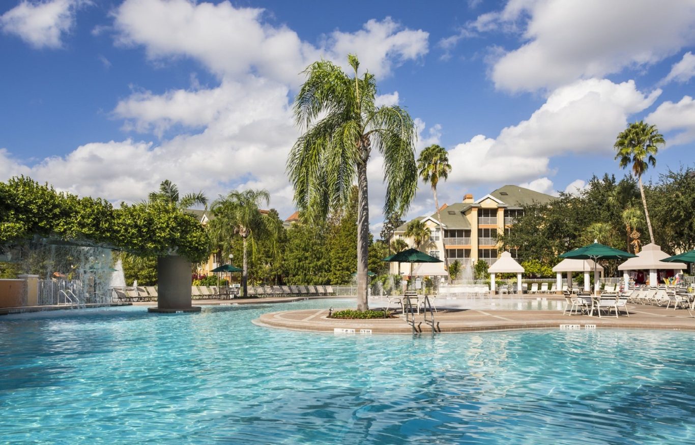 Serene resort pool with palm trees and sun loungers under a blue sky.