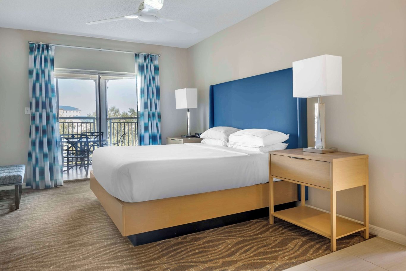 A bright, modern hotel room featuring a king-sized bed and balcony view.