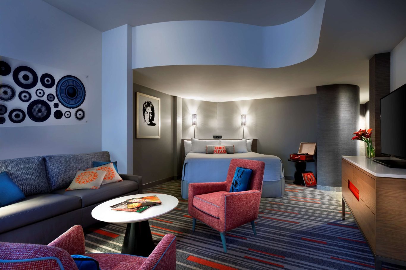 Modern hotel room with a seating area, bed, and stylish decor in muted tones.