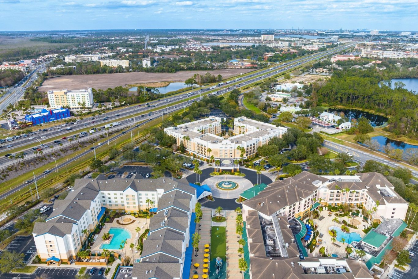 Aerial view of residential buildings with pools near a highway and green areas.