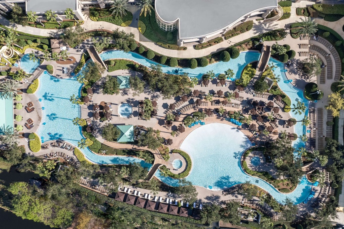 Aerial view of a resort with multiple blue pools and sun loungers surrounded by greenery.