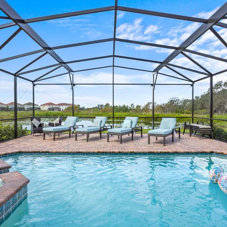 Lounge area with chairs around a pool, enclosed by a mesh screen and surrounded by greenery.