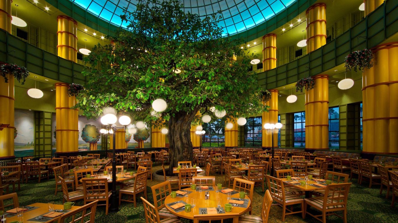 Spacious restaurant interior with wooden furniture and a large central tree.