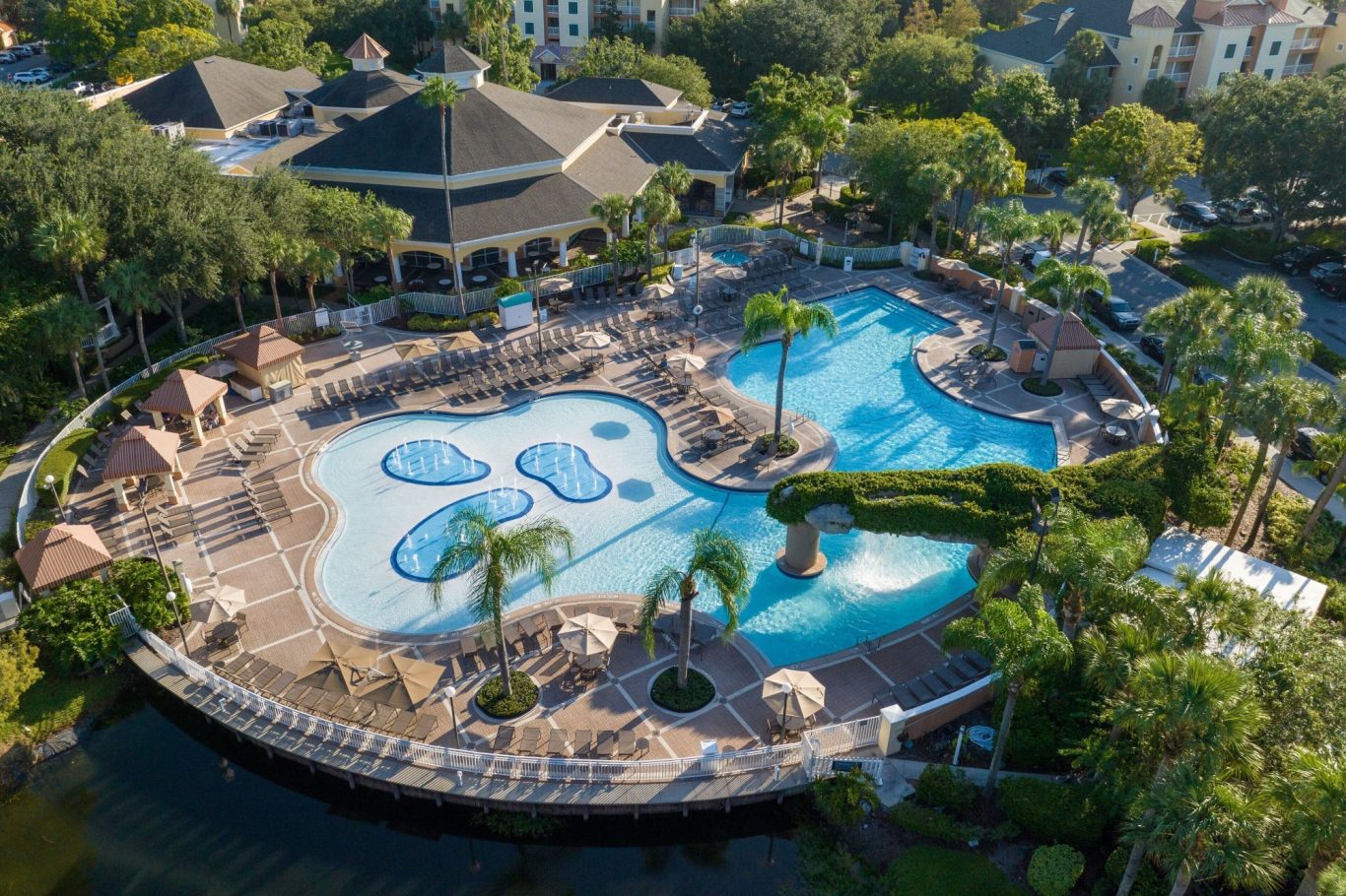 Aerial view of a large resort pool area with palm trees and lounging chairs.