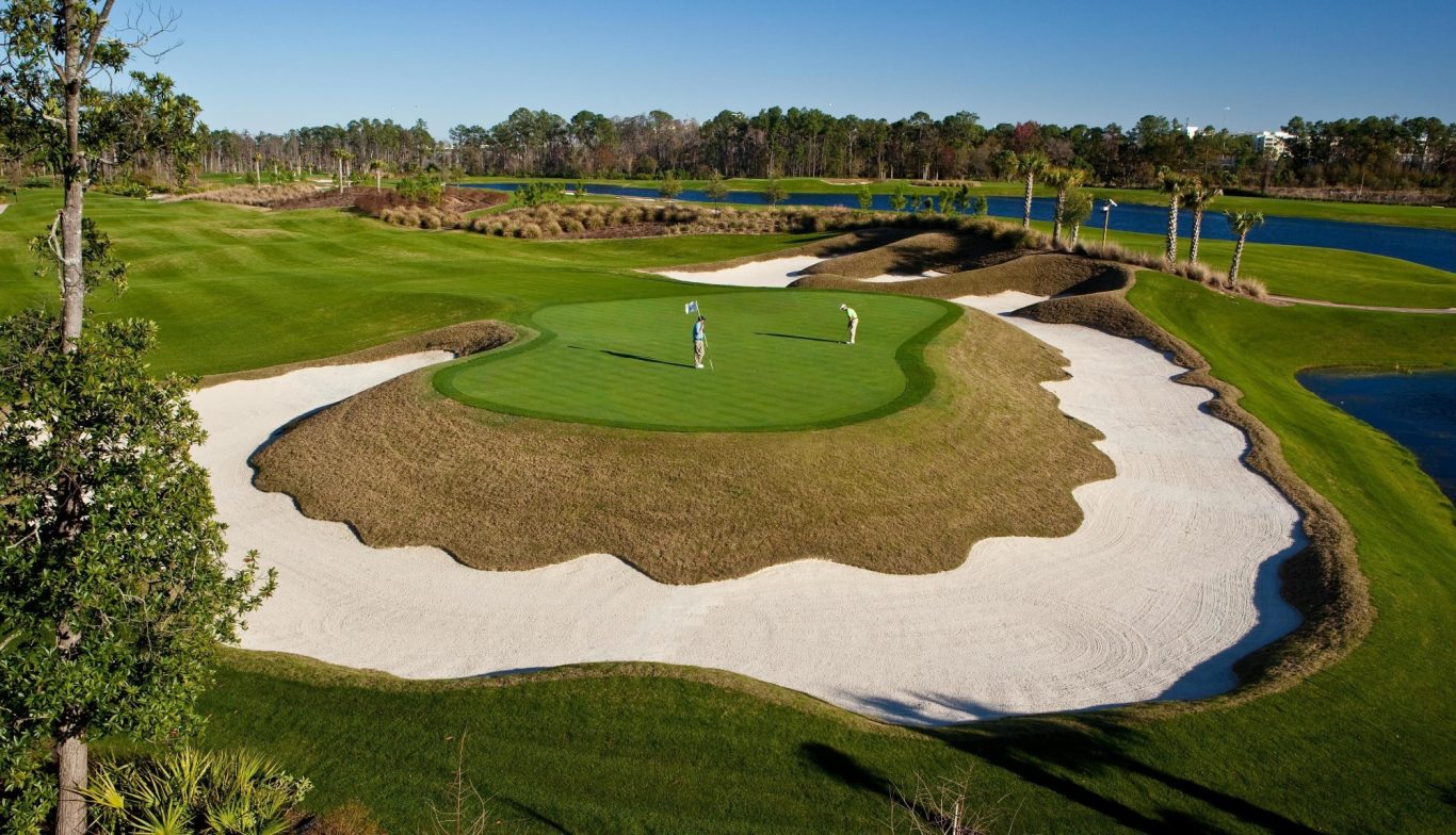 A golf course green surrounded by sand traps and water features on a sunny day.