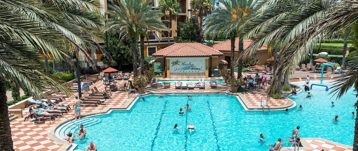 A pool area surrounded by palm trees, with people relaxing and swimming.