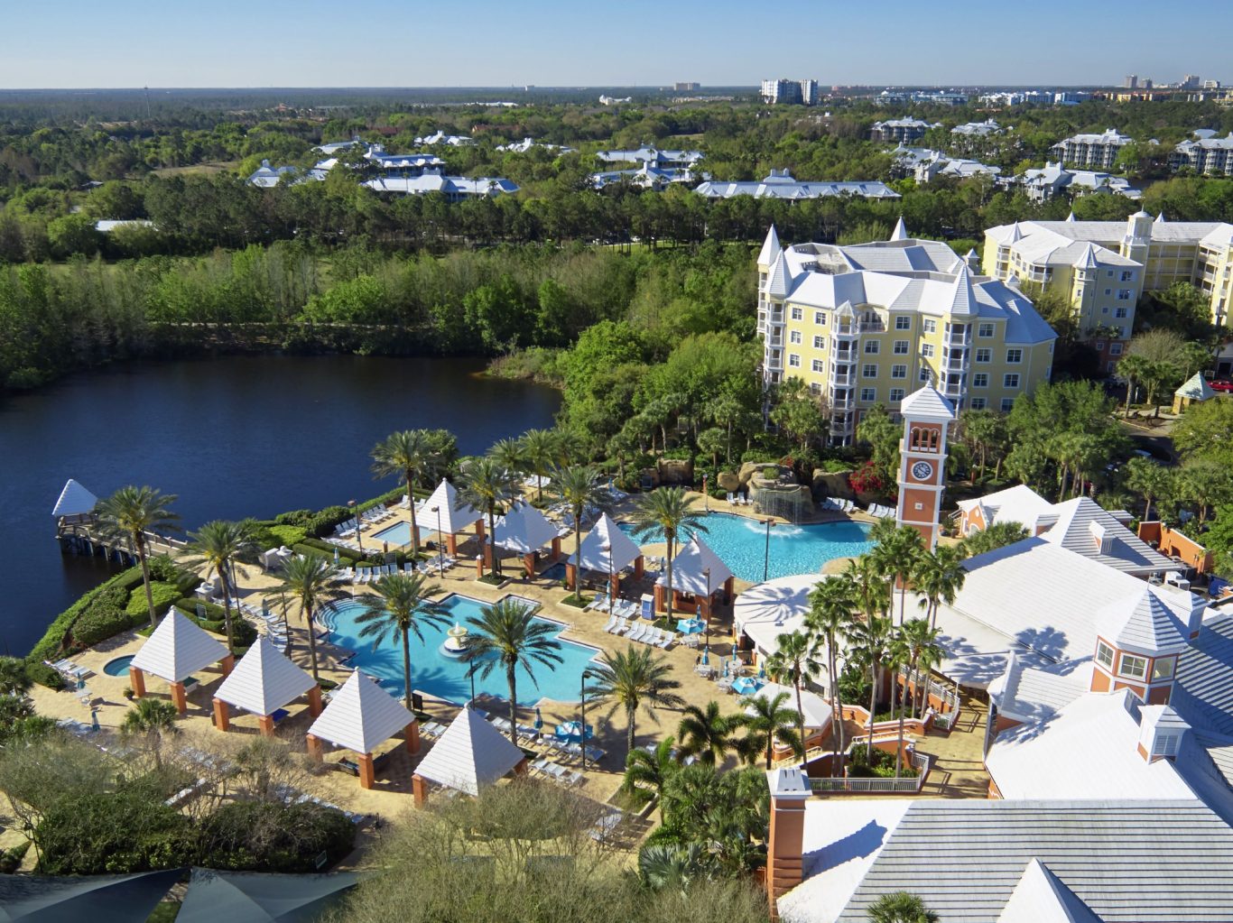 Aerial view of a resort with pools, cabanas, and landscaped gardens near a water body.