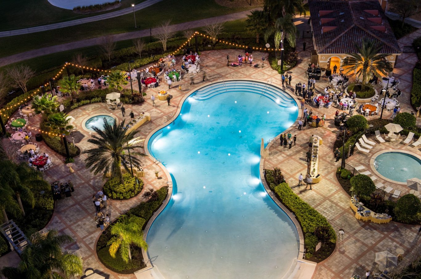 Aerial view of a pool area with lush landscaping and social gathering at night.