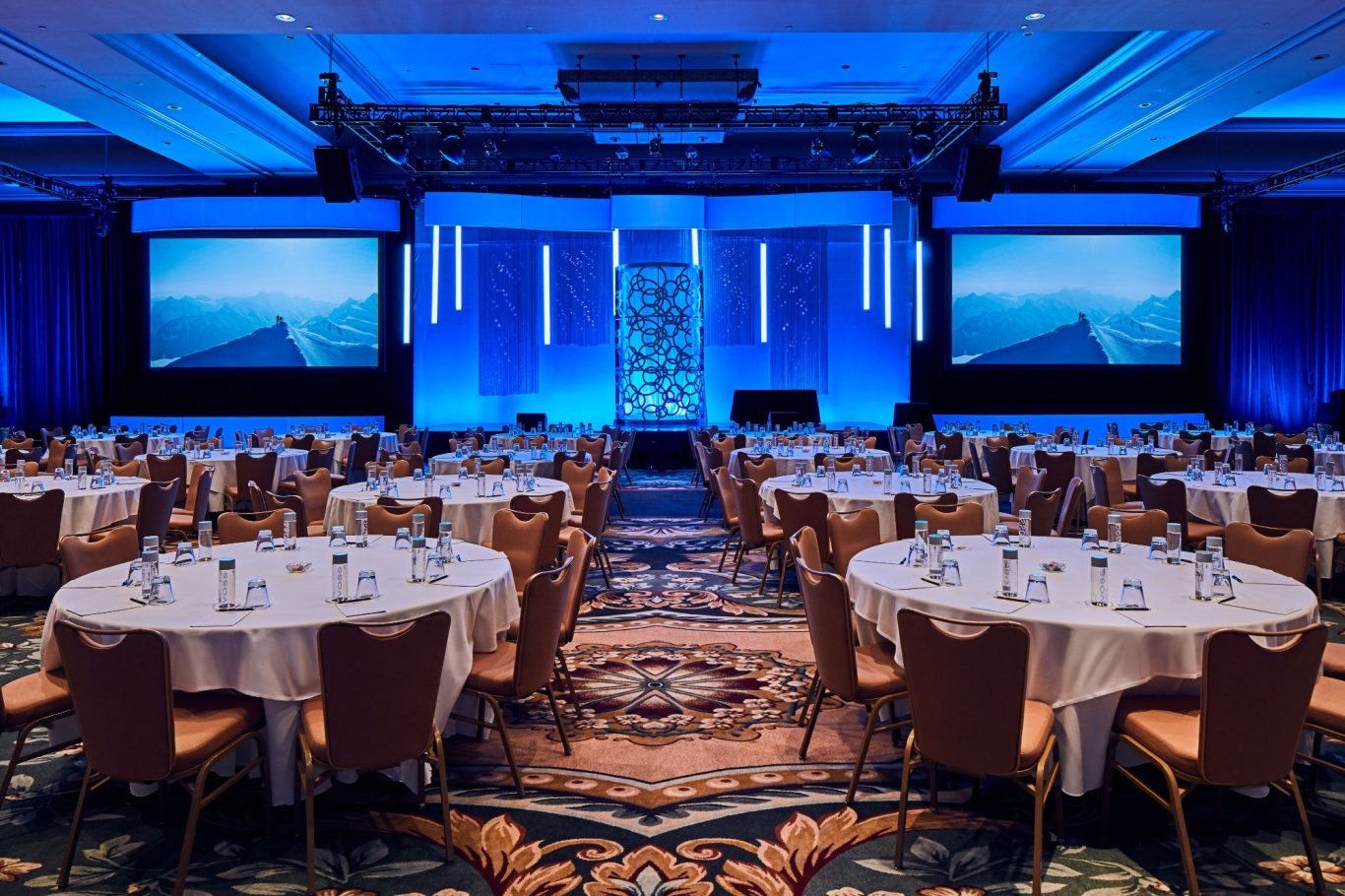 Conference hall set up with round tables, blue lighting, and a stage at the front.