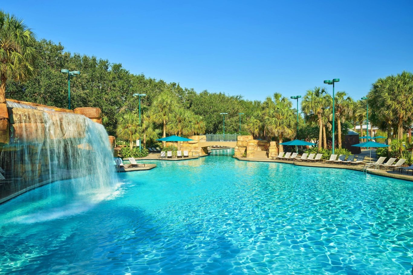 Crystal-clear pool with a waterfall, surrounded by palm trees and lounge chairs.