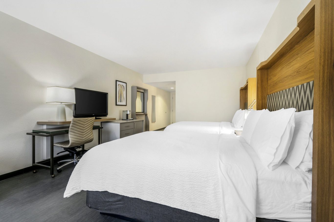 Modern hotel room with two beds, a work desk, and a TV.