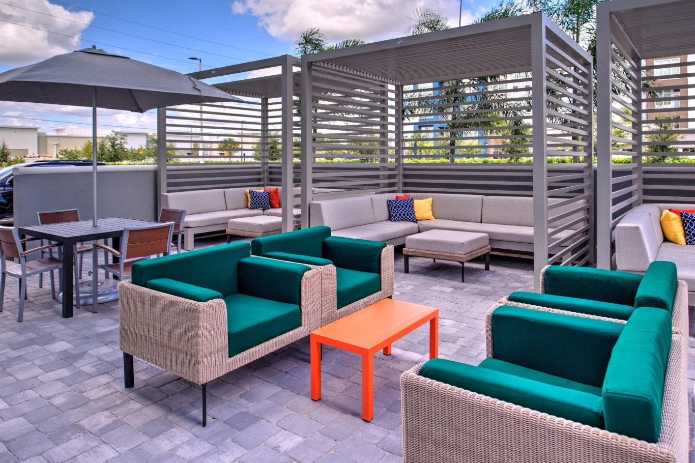 Outdoor seating area with green sofas, orange table, and shaded lounge space.