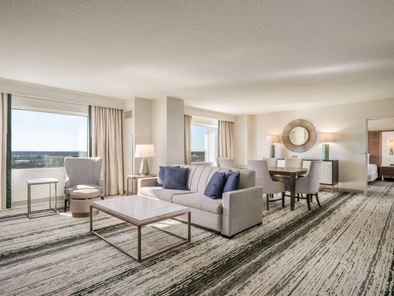 Bright, spacious hotel room with a sofa, dining area, and large windows overlooking the city.