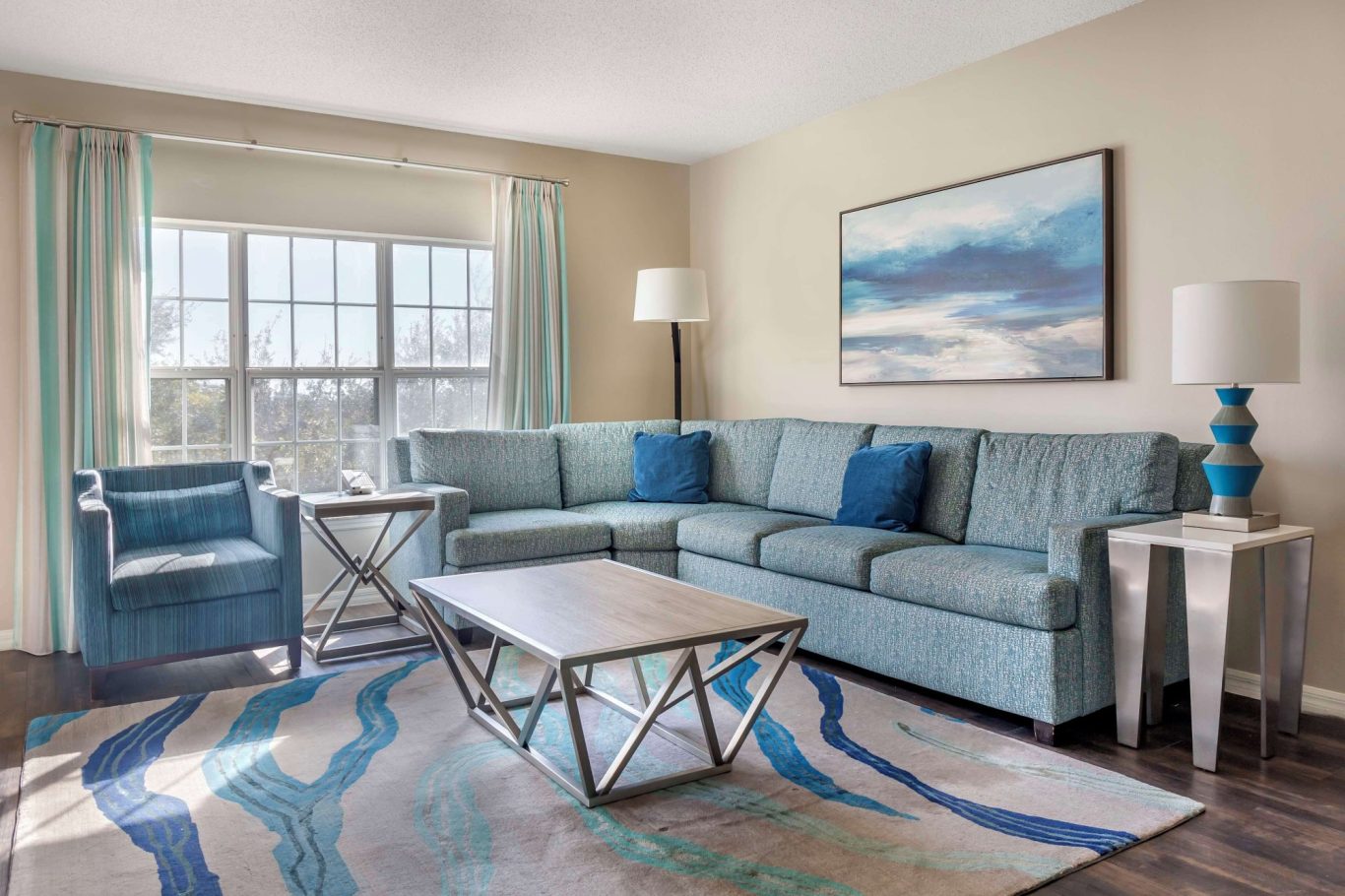 Bright living room featuring a blue sofa, armchair, and a decorative rug with waves.