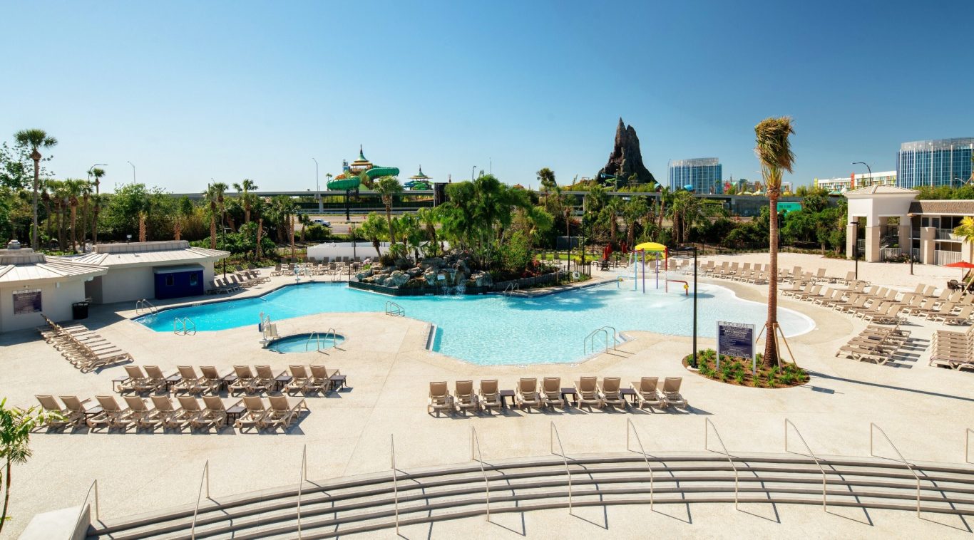 Resort pool area with sun loungers and tropical landscaping under a clear blue sky.