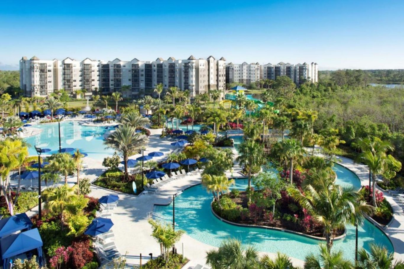 Luxury resort featuring lush landscaping, pools, and modern buildings under a clear blue sky.