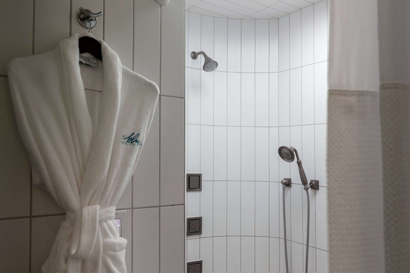 A white bathrobe hanging next to a modern shower with tiled walls.