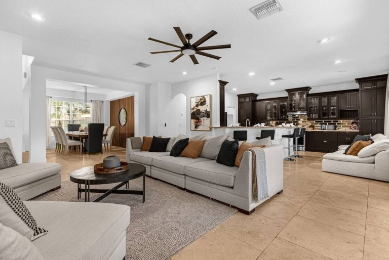 Spacious living room with light furniture, a round table, and a modern kitchen in the background.